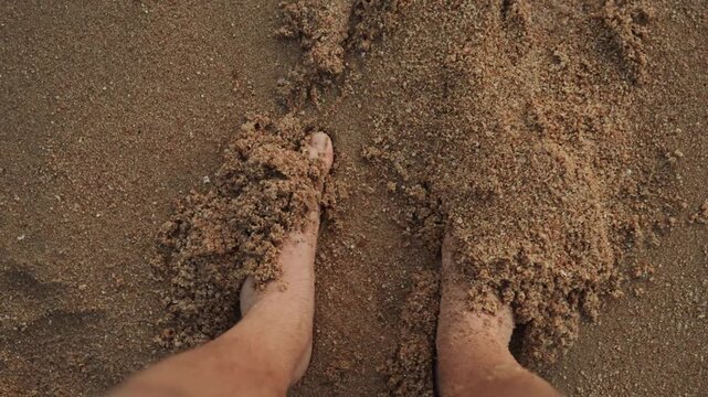 Bare feet buried in sand, traveler grounding on warm beach closeup of toes and textured grains, sunset glow, slow meditative movement, wellness ritual and peaceful seaside solitude.