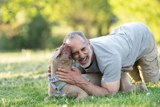 An older man loving on his dog in the yard.