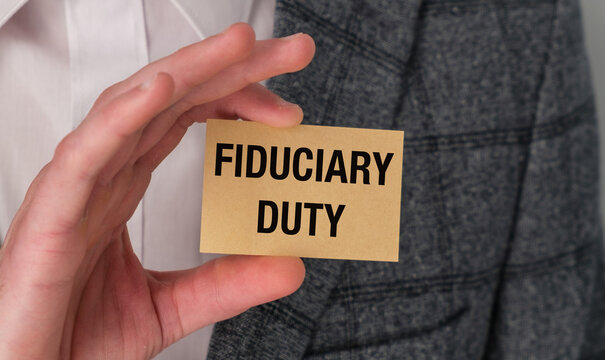 Hand holds sign saying Fiduciary Duty. Business attire suggests professionalism and responsibility.