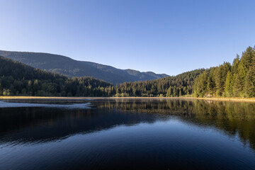 Fototapeta premium Scenic view of mountains and forest reflecting in a calm lake at Minnekhada Regional Park Coquitlam Canada