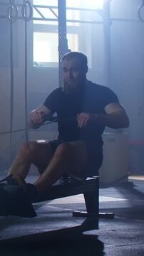 Focused athlete training on indoor rowing machine in dimly lit gym, demonstrating intense full body workout, endurance exercise and functional fitness conditioning