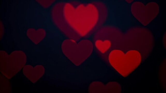 Soft glowing red hearts gently float and pulse against a dark romantic background for love and Valentine
