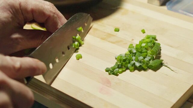 Macro shot of a professional chef cutting fresh green onions with a knife on a bamboo cutting board