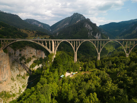 Aerial drone view of the historic Durdevica Tara Bridge, a concrete arch bridge over the Tara River Canyon in northern Montenegro. Lush green mountains and deep canyon landscape.