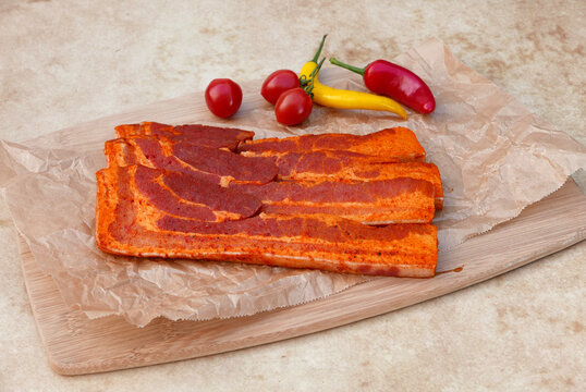 Marinated pork belly slices with chili and tomatoes on a rustic wooden board.