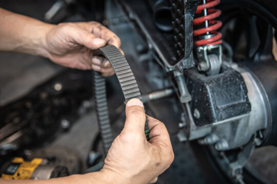 Mechanic hands inspecting a worn motorcycle drive belt for CVT transmission service.