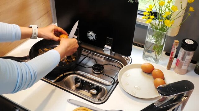 Woman Cracking Egg into Frying Pan with Mushrooms in RV Kitchen.