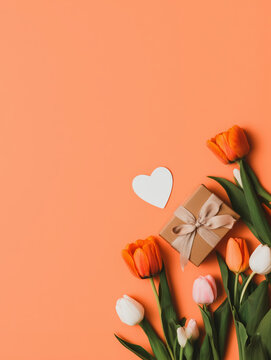 Orange tulips and gift box on coral background with copy space