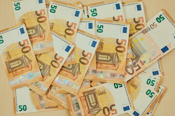 Obraz premium Fifty euro banknotes are scattered across a wooden surface in a layered cash pattern. Mid value currency concept for payment, budgeting, retail and consumer finance.