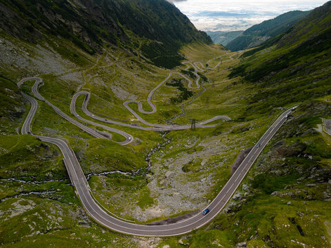 Aerial drone view of the famous Transfagarasan highway in the Fagaras Mountains, Romania. Winding serpentine road with cars driving through a green mountain valley under a cloudy sky.