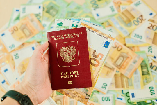 Hand holds Russian passport over euro banknotes background for travel and relocation concept. Immigration planning with document, European currency and vacation budget.