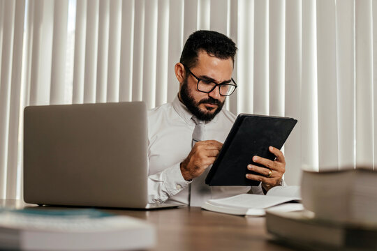 Businessman using tablet at desk, browsing and managing digital tasks in a modern office environment with focus and concentration.