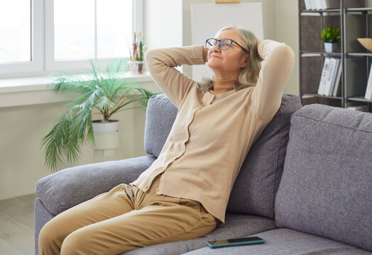 Happy senior woman resting and relaxing on sofa at home, enjoying positive grandmother moments, enjoyment in a quiet nook designed for senior leisure and comfortable relaxation time.