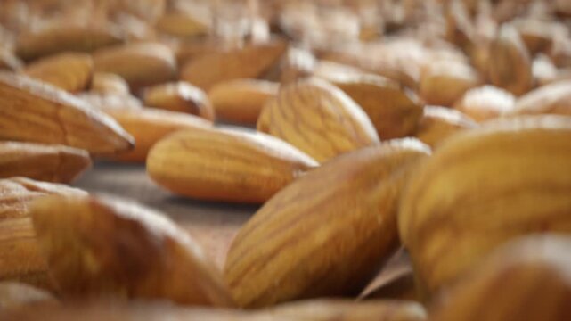 Scattered almonds settle into a loose cluster on wooden surface in shallow focus with forward camera drift