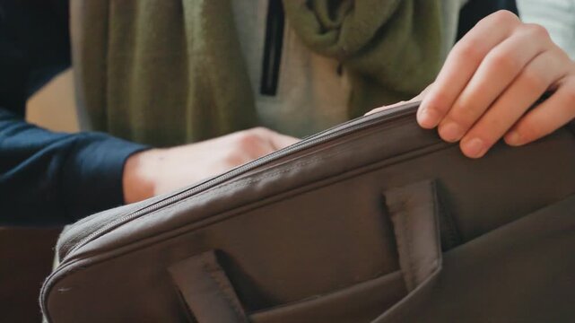 Caucasian man zips laptop bag while seated indoors, closeup on hands and zipper, canvas briefcase and strap adjusted, focused prep for urban transit, quick departure mood with textured fabric and soft