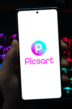 Punta Arenas, Chile &ndash; May 04, 2026: Close-up of a mobile device screen showing the Picsart photo and video editing application logo, held by a user in a dimly lit room with vibrant RGB keyboard 