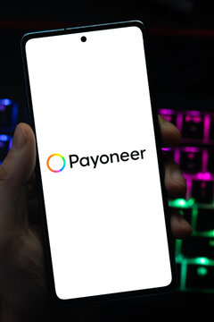 Punta Arenas, Chile &ndash; May 04, 2026: Close-up of a mobile device screen showing the Payoneer financial services platform logo, held by a user in a dimly lit room with vibrant backlit keyboard lighting