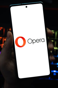Punta Arenas, Chile &ndash; May 04, 2026: Close-up of a mobile device screen showing the Opera web browser logo, held by a user in a dimly lit room with vibrant RGB keyboard lighting