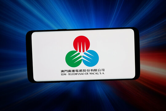 Stuttgart, Germany - 04-23-2026: In this photo illustration, the logo of TV company TDM - Teledifusao de Macau S. A. is displayed on a smartphone in front of abstract background on computer screen.