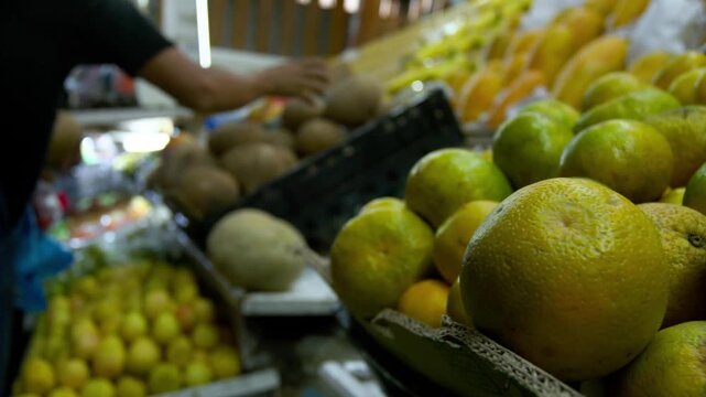 Naranjas y frutas tropicales en mercado local con personas de fondo - 4K