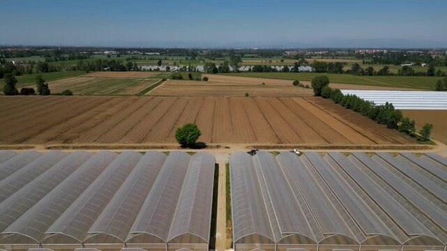 Agricultural Fields and Greenhouses: An aerial view showcases expansive agricultural fields, some tilled and brown, others green and ready for harvest, alongside modern greenhouses.