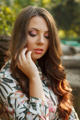 Fototapeta premium A young woman with long brown hair poses thoughtfully outdoors