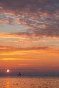 Calm Ocean Sunset With Distant Ship Silhouette and Scenic Sky Cloudscape Over Water