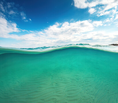 Half underwater view of crystal clear turquoise sea water and paradise exotic island with beach and rocks on the coast on a nice sunny day Greece