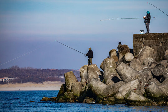 Fishermen on a concrete breakwater by the sea on a cool day