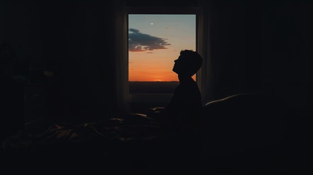 Person silhouette waking up in dark bedroom looking at sunrise through window contemplation concept