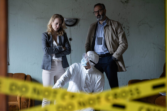 Forensics team, detectives, and investigators working at a crime scene, analyzing evidence behind yellow do not cross tape