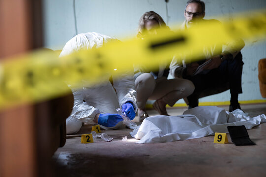 Crime scene investigators in protective suits collecting fragments of broken glass and evidence markers on the floor, solving murder mystery