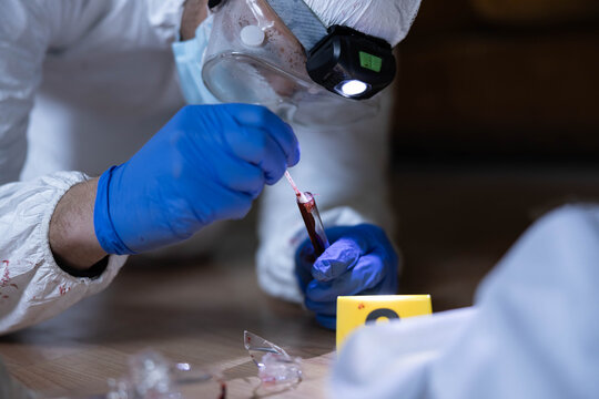 Forensic investigator in protective suit and gloves collecting blood evidence from a test tube for dna analysis, working late