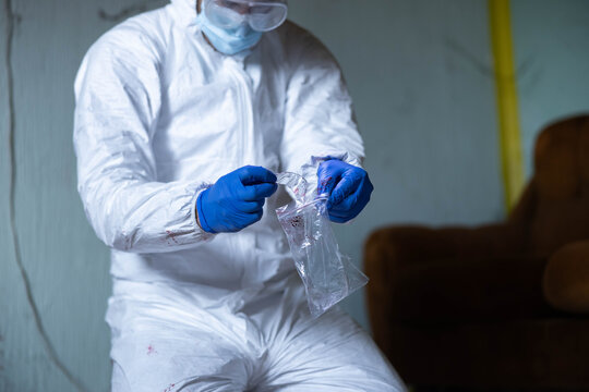 Forensic specialist in protective suit and gloves collecting a blood sample into an evidence bag during a crime scene investigation