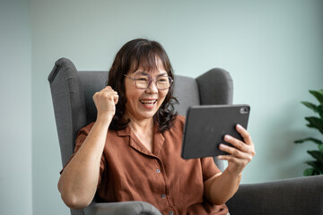 Naklejka premium Happy senior woman using tablet at home with digital technology engagement lifestyle, older female texting and online connected with family, retired communication in daily life with wellbeing at home