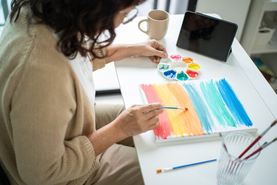 Smiling pretty senior asian woman painting and coloring on a canvas at home with creative lifestyle and healthy aging with mental wellness for retirement, elderly female enjoy leisure activity