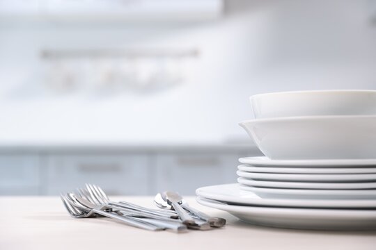 Clean dishes on white table in kitchen, closeup. Stack of bowls, plates and cutlery
