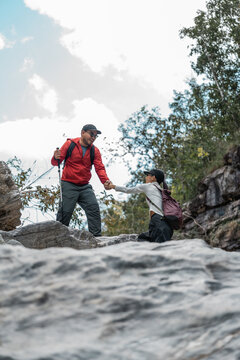 Couple Hiker man and woman climbing rocky mountain to explore cave hill and river enjoying outdoor adventure trekking, and nature travel. Two traveller and nature lover on an exciting hiking journey
