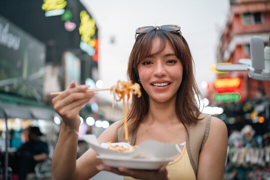 Young woman enjoy eating street food at night market. Traveler blogger women Happy tourists Beautiful female with Traditional food local road at thailand bangkok city.