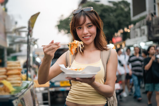 Young woman enjoy eating street food at night market. Traveler blogger women Happy tourists Beautiful female with Traditional food local road at thailand bangkok city.