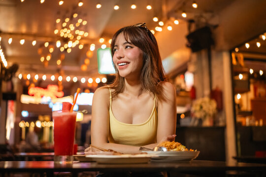 Young woman enjoy eating street food at night market. Traveler blogger women Happy tourists Beautiful female with Traditional food local road at thailand bangkok city.