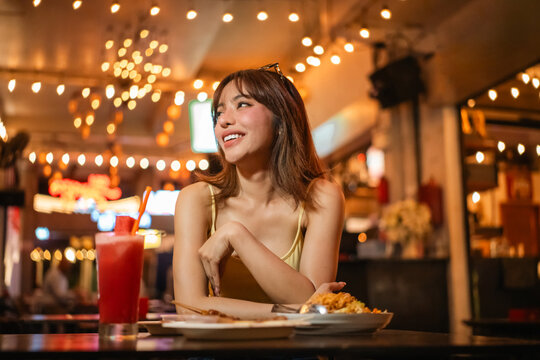 Young woman enjoy eating street food at night market. Traveler blogger women Happy tourists Beautiful female with Traditional food local road at thailand bangkok city.