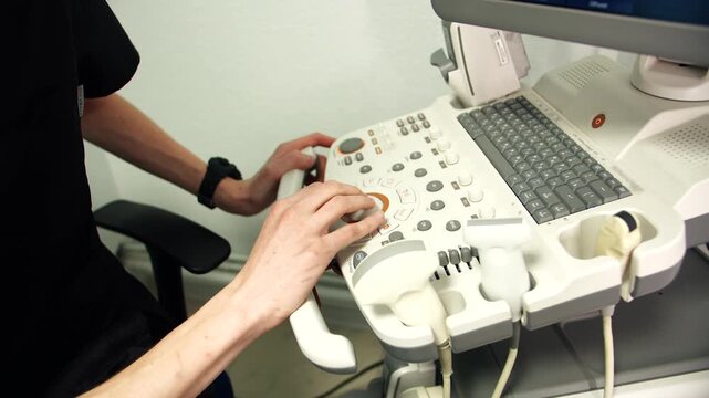 Male hands skillfully operating ultrasound console in clinic, caucasian sonographer adjusts probe settings and captures diagnostic images. Closeup of keyboard, knobs, transducer cables and sensors