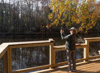 Fototapeta premium Woman standing on a dock in nature taking a smart phone photo