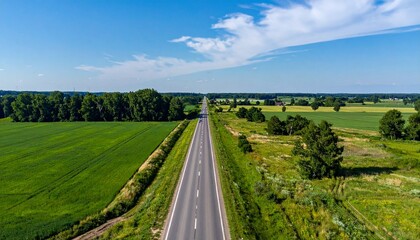 Fototapeta premium Open road through green countryside with clear sky. Clean travel and infrastructure concept with natural landscape.