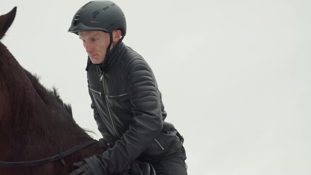 Rider adjusts bridle and helmet closeup with focused hands fastening strap and checking saddle, intimate winter detail shot highlighting safety, gear and tactile bond before ride in muted outdoor