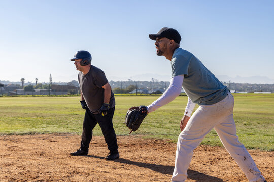 Two male players crouching on dirt infield at neighborhood field, holding glove and batting helmet