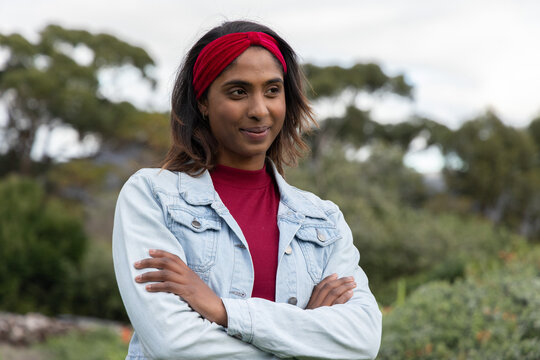 Indian woman standing with arms crossed in park wearing red headband red top denim jacket