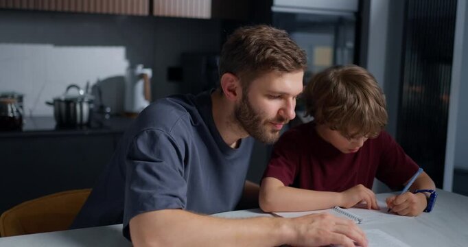 White Male Parent Provides Attentive Guidance To Son Over School Assignment At Kitchen Table