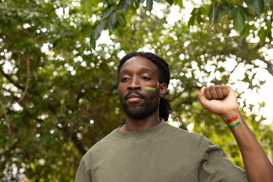 African man raising fist in woods, wearing olive shirt, showing tricolor cheek and wrist paint